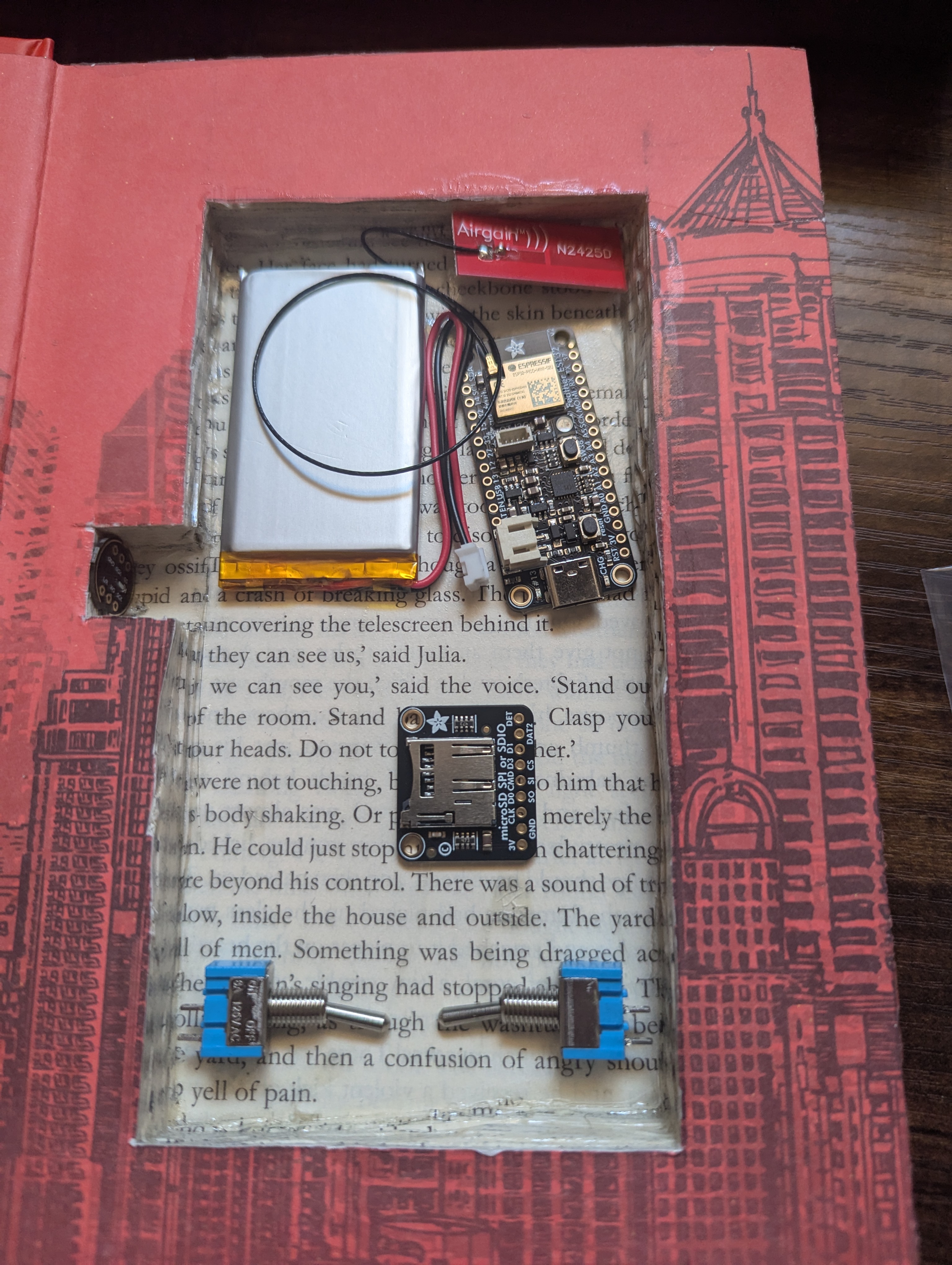 Components test-fit into book cavity — battery, Feather ESP32, and SD breakout visible